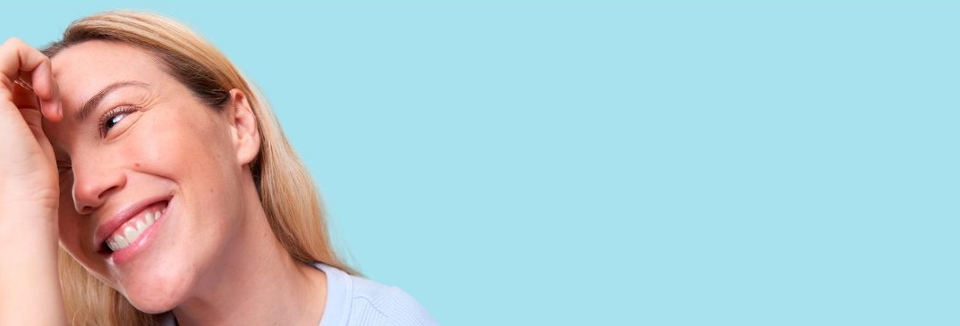 Mujer sonriendo con piel luminosa y radiante, reflejando bienestar y una rutina de skincare equilibrada con fondo azul claro